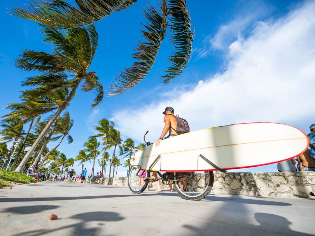 Man riding a bike with a surfboard attached in South Beach Miami